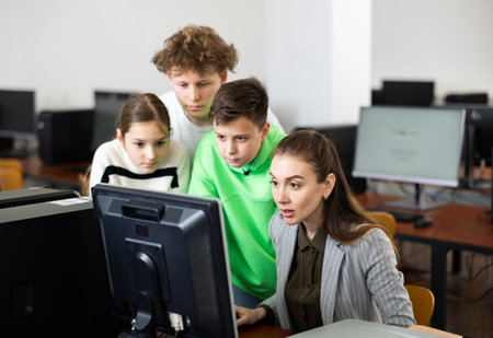 Female teacher and teenager pupils looking at monitor of PC
