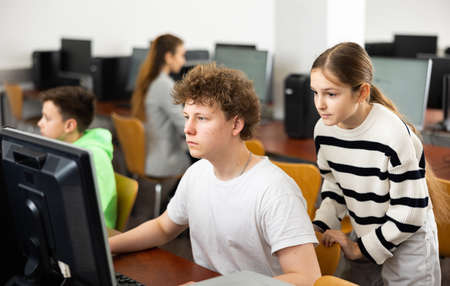 Teen schoolgirl talking to focused classmate in computer classの写真素材