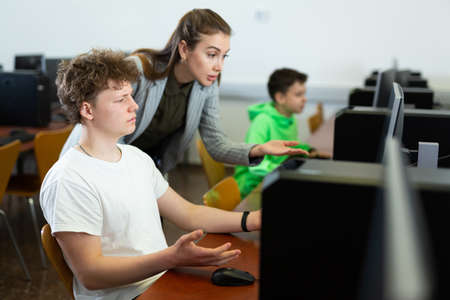 Female teacher helping focused teenage student in computer labの写真素材