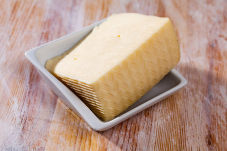 Delicious slice of semi-soft cheese on a wooden table