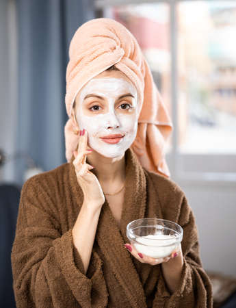 Portrait of woman in bathrobe with face covered with creamの写真素材