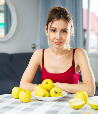Portrait of young woman sitting at table and eating applesの写真素材