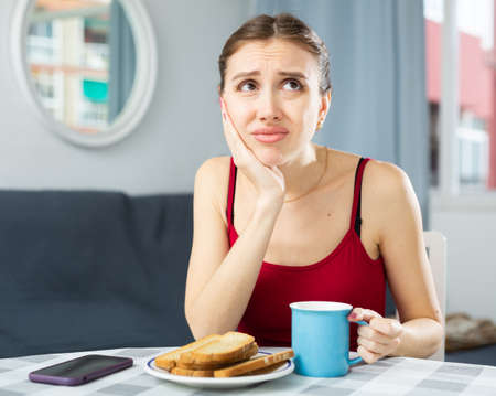 Woman having toothache, sitting at table at homeの写真素材