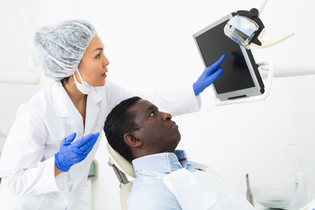 Woman dentist pointing at display to show information to patientの写真素材