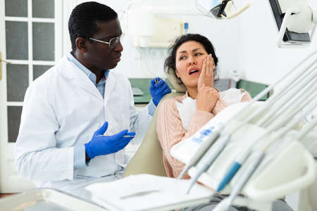 Woman patient who came to an appointment with a male dentist is sitting in a dental chair in clinic office, showing which side of her tooth achesの写真素材