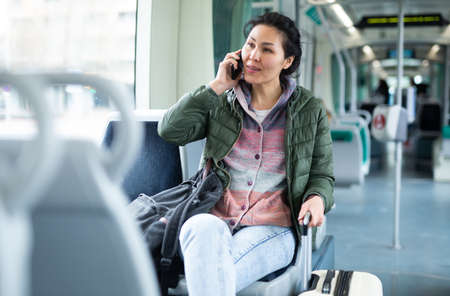 Oriental woman talking on mobile phone while riding a tramの写真素材