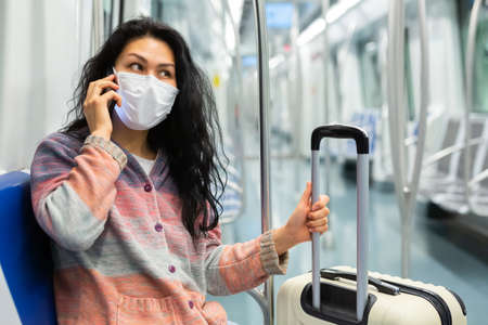 Woman traveler in a protective mask talking on a mobile phone in subway carの写真素材