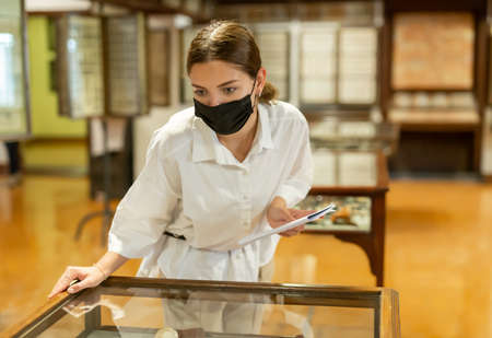 Young woman in mask with booklet visiting archaeological museumの写真素材
