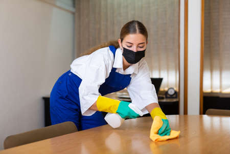 Female cleaning service worker in protective mask wiping desk in officeの写真素材