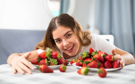 Portrait of a young woman sitting at a table with strawberriesの写真素材