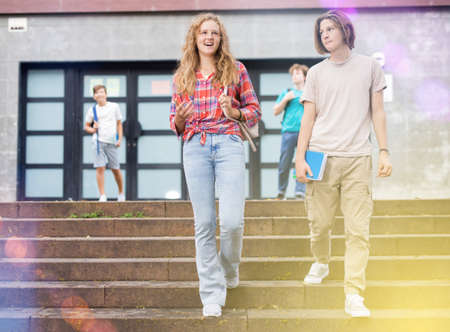 Smiling teenagers boy and girl walking home after finishing college lessons on dayの写真素材