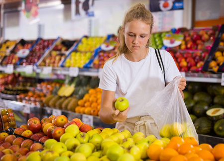 Young woman purchaser choosing apples in groceryの写真素材
