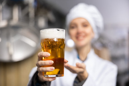Glass of foamy amber ale in hands of female brewerの写真素材