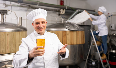 Cheerful man brewer presenting glass of beer