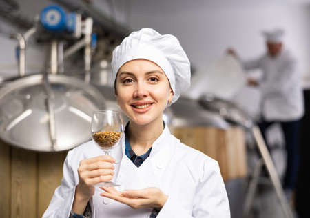 Portrait of positive female brewer with a glass of barley at breweryの写真素材