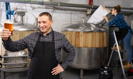 Portrait of positive man brewmaster with glass of beer