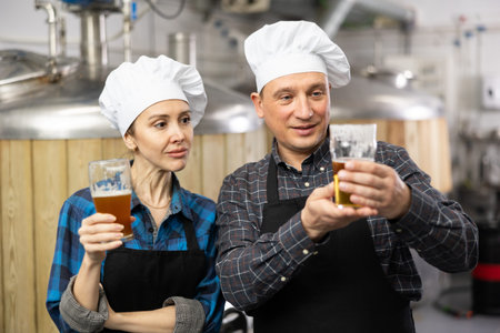 Man and woman brewers looking at glass of beer
