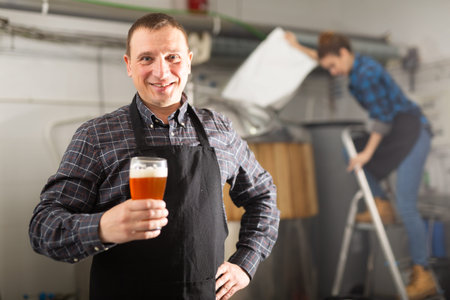Portrait of positive man brewmaster with glass of beer
