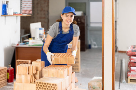 Young woman builder stacking bricks in building site