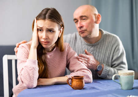 Man comforting his sad wife sitting at tableの写真素材