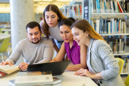 Friendly group of students preparing together for exam in modern university libraryの写真素材