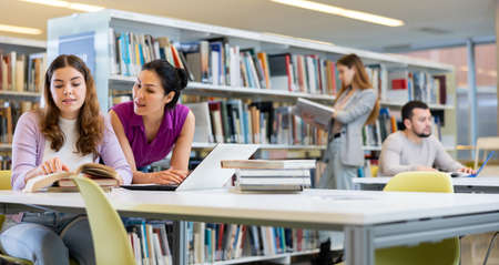 Two female students preparing a report on a laptop in the libraryの写真素材