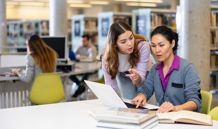 Caring woman helping friend to prepare for exams in library