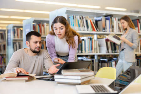 Man working with female colleague on joint project in libraryの写真素材