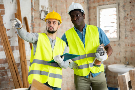 Two builders talking on indoor construction site
