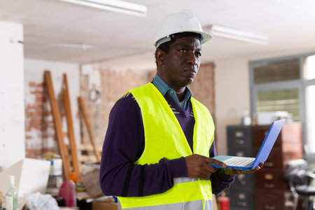 African american supervisor with laptop inspecting construction site