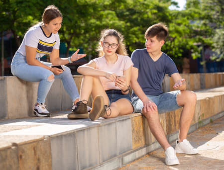 Teenagers friendly discussing and using phones outdoorsの写真素材