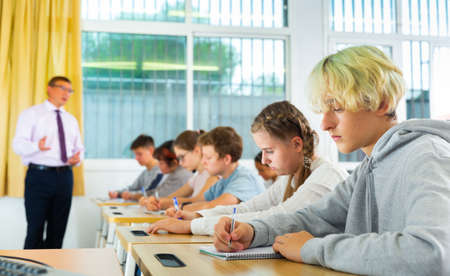Side view of student group working on lecture in classroomの写真素材