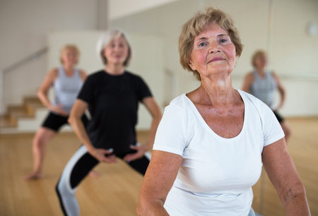 Mature women perform a plie squat while in the position of a ballet stand