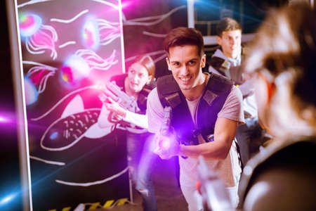 Portrait of happy young man with laser pistol and playing laser tag with his friends in dark roomの写真素材