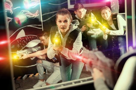 Portrait of excited woman holding laser gun in arena, playing laser tag game with friends