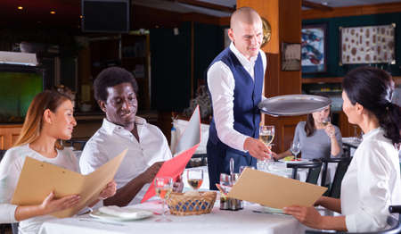 Polite waiter bringing ordered drinks to restaurant guestsの写真素材