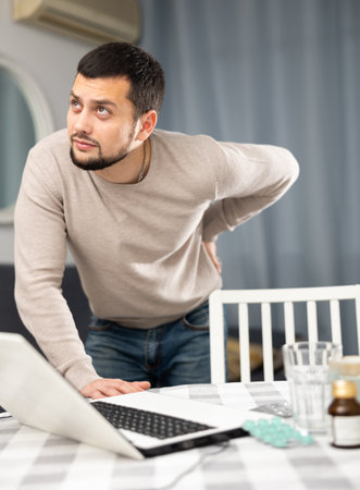 Man experiencing severe back pain after working long hours on laptopの写真素材