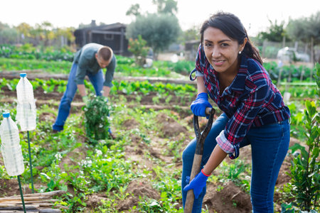 Woman gardener holding shovel in garden against background of working peopleの写真素材