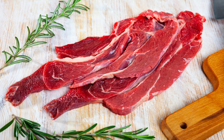 Unfinished beef steak with sprig of rosemary on cutting board