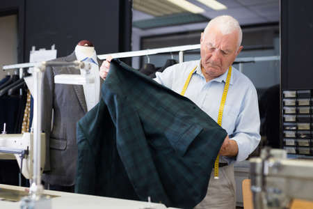 Professional tailor inspects mens jacket before starting work in workshopの写真素材