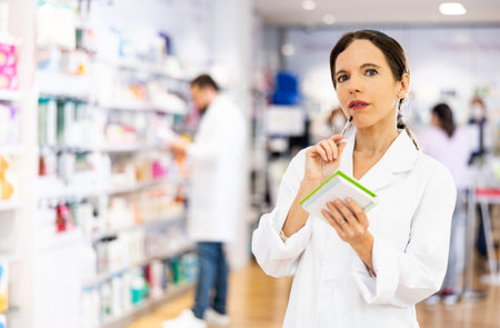 Woman pharmacist checking medicines, making notes in drugstoreの写真素材
