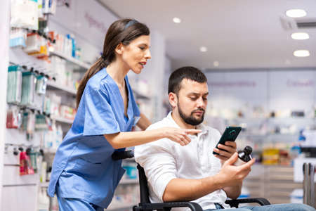 Woman pharmacist helping man in wheelchair to help choose medicineの写真素材