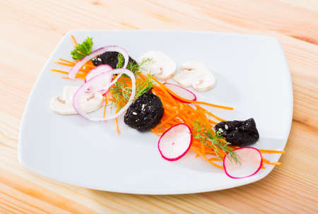 Vegetarian dish, salad from carrot, radishes and prunes served at plateの写真素材