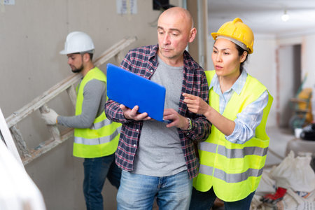 Man with laptop taking to female forewoman in apartment during renovation