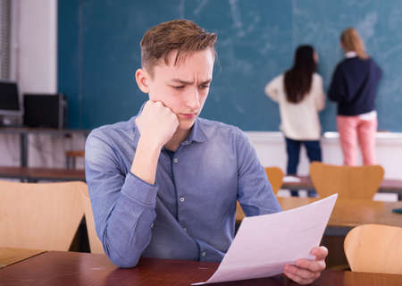 Young thoughtful guy preparing for the exam in classroomの写真素材