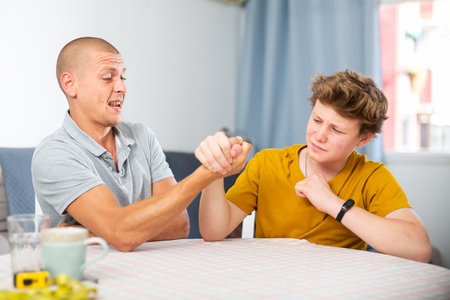 Happy smiling father and son arm wrestling at homeの写真素材