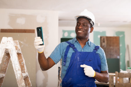 African-american man construction worker holding document in hand while standing in building site,...