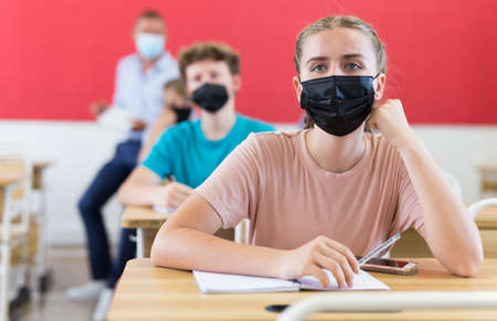 Young students in face masks sitting at desks in classroomの写真素材