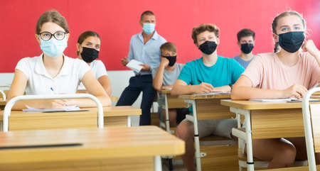 Teenager students in masks sitting at desksの写真素材