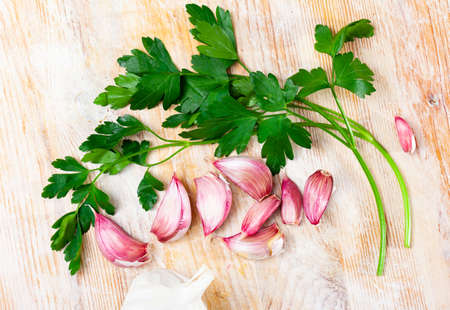 Cutting board with fresh seasonings on a wooden background. White garlic heads and cloves and parsley leavesの写真素材